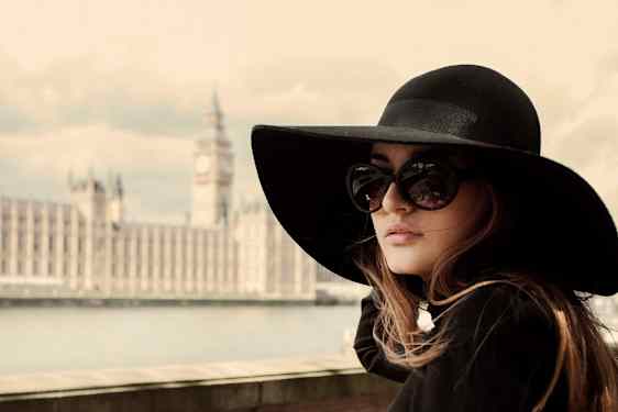 En person med en stor svart hatt står vid en flod med Westminsterpalatset och Big Ben i bakgrunden. (AI-genererad text)