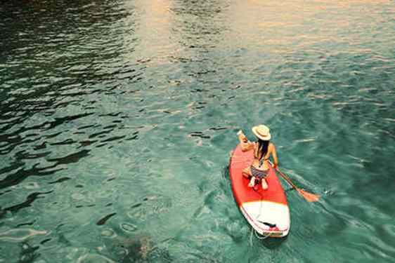 Person som står upp på en bräda och paddlar i solnedgången