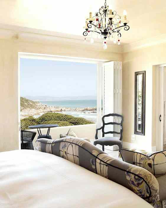 Ett ljust sovrum med en dubbelsäng, sittmöbler och en öppen balkong med utsikt över havet. (AI-genererad text)