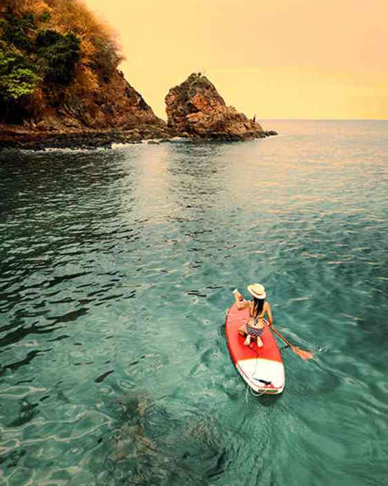 Person som står upp på en bräda och paddlar i solnedgången