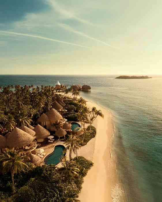 Flygbild av en tropisk strand med vit sand, palmer och bungalowliknande byggnader bredvid en pool. (AI-genererad text)