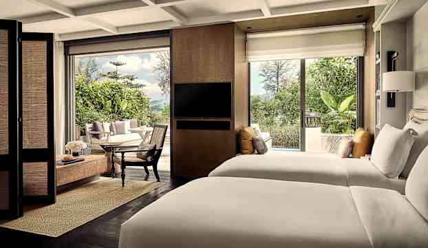 Ett hotellrum med två sängar, sittgrupp och en modern inredning, samt utsikt mot en grön trädgård utanför. (AI-genererad text)