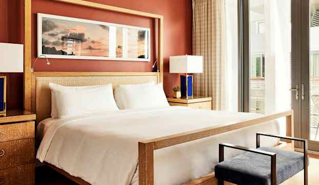 Ett stilfullt hotellrum med en stor säng, nattygsbord med lampor och en väggmålning ovanför sängen. (AI-genererad text)