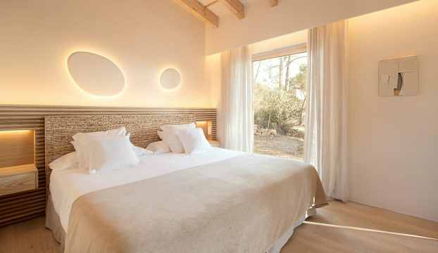 Ett sovrum med en dubbelsäng, vita sängkläder och mjukt dekorativt ljus på väggen. (AI-genererad text)