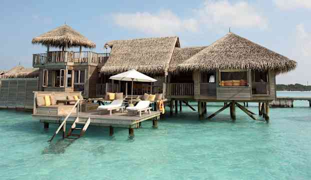 En bungalow med halmtak står på pålar i turkosfärgat vatten. (AI-genererad text)