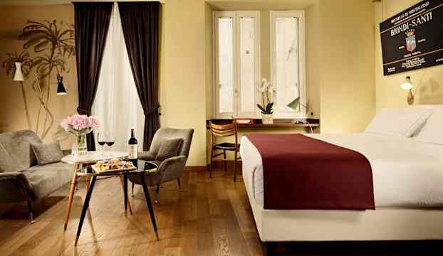 Ett hotellrum med en säng, sittgrupp och ett bord med vin och blommor. (AI-genererad text)