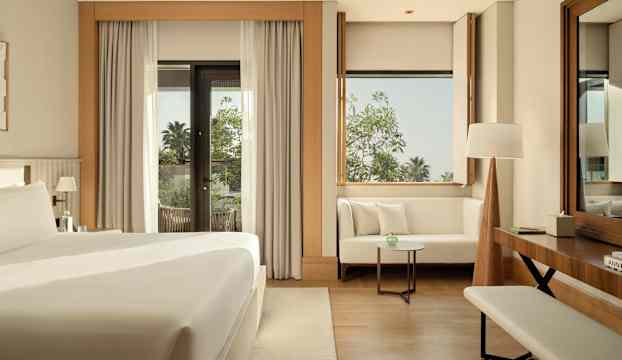 Ett modernt hotellrum med en stor säng, sittgrupp och en balkong med utsikt över grönska. (AI-genererad text)