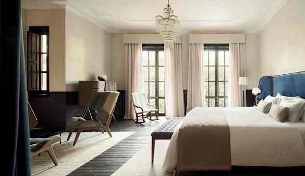 Ett ljust sovrum med en stor säng, stolar och fönster med gardiner. (AI-genererad text)