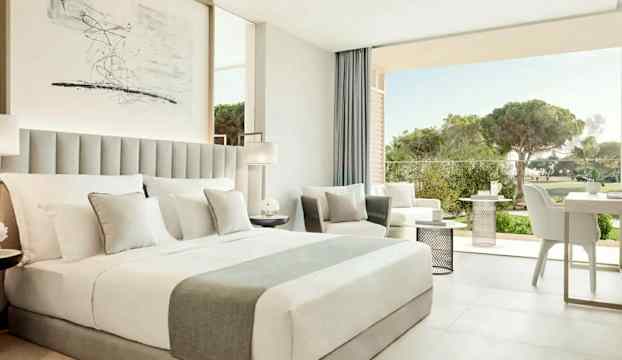 Modernt hotellrum med en stor säng, sittgrupp och balkong med utsikt mot naturen. (AI-genererad text)