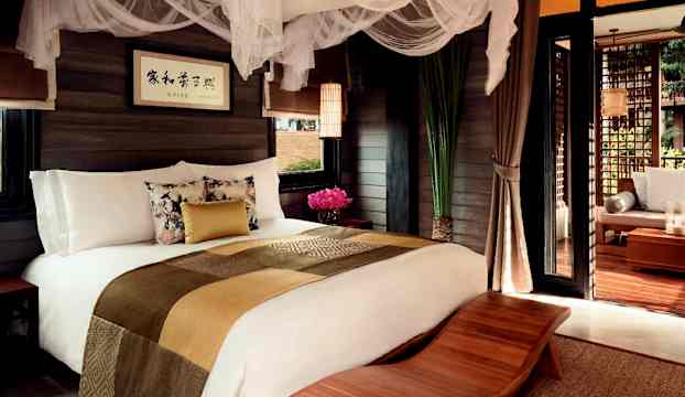 Ett sovrum med en stor bekväm säng, dekorerad med sängöverkast och kuddar, samt nät ovanför sängen. (AI-genererad text)