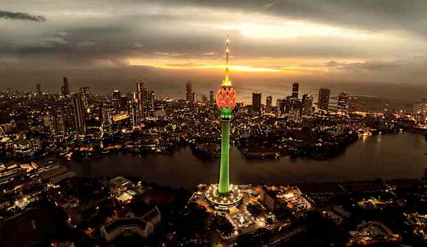 En stad med höghus och en upplyst tornstruktur vid solnedgången. (AI-genererad text)