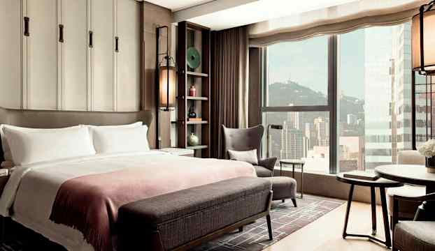 Ett hotellrum med stor säng, sittmöbler och utsikt mot en stad genom fönstret. (AI-genererad text)