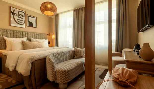 Ett välmöblerat hotellrum med en stor säng, en sittmöbel, ett bord och väggdekorationer. Fönstren är täckta med gardiner. (AI-genererad text)