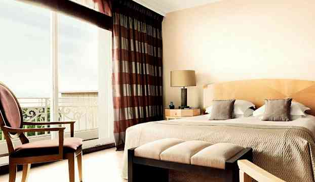 Ett hotellrum med en dubbelsäng, en stol, en ottoman och stora fönster med utsikt. (AI-genererad text)