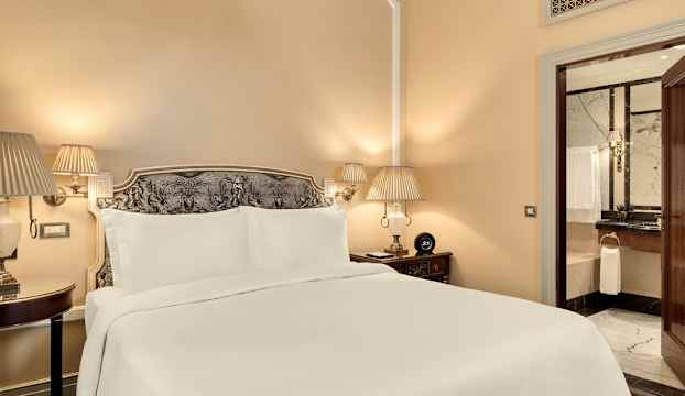 Bild på ett hotellrum med en bred säng, nattduksbord och en dörr till ett badrum. (AI-genererad text)