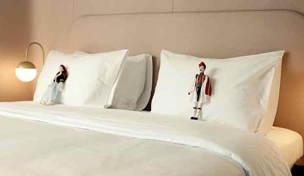 En bäddad hotellsäng med två dekorerade dockor placerade på vita kuddar. (AI-genererad text)