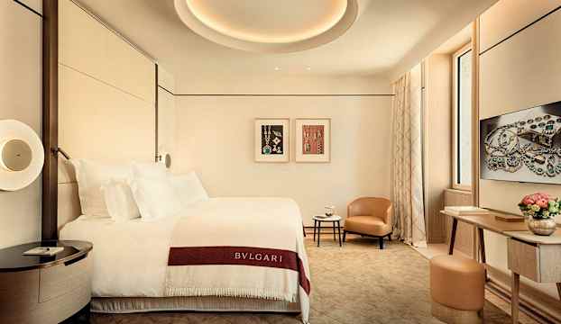 Ett elegant hotellrum med en bäddad säng, sidobord, fåtölj och ett arbetsbord. (AI-genererad text)