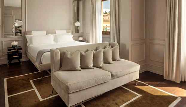 Ett elegant hotellrum med en bred säng och en sittmöbel framför. Rummet är inrett i ljusa toner och har stora fönster. (AI-genererad text)