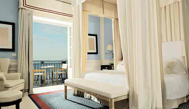 Ett elegant hotellrum med himmelssäng, sittmöbler och utsikt mot havet. (AI-genererad text)