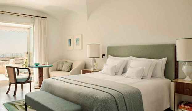 Ett ljust och elegant inrett hotellrum med en dubbelsäng, sittgrupp och en balkong. (AI-genererad text)