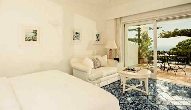 Ljus hotellrum med soffa, säng och öppna fönster mot balkong. (AI-genererad text)