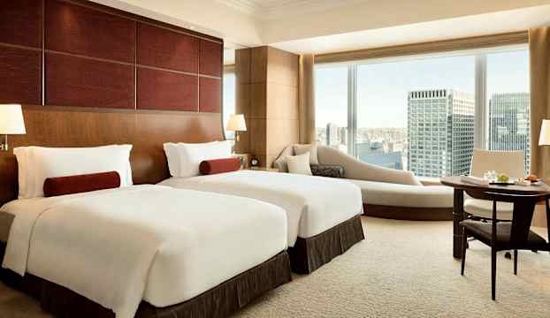 Ett hotellrum med två enkelsängar, en sittgrupp med utsikt över staden. (AI-genererad text)