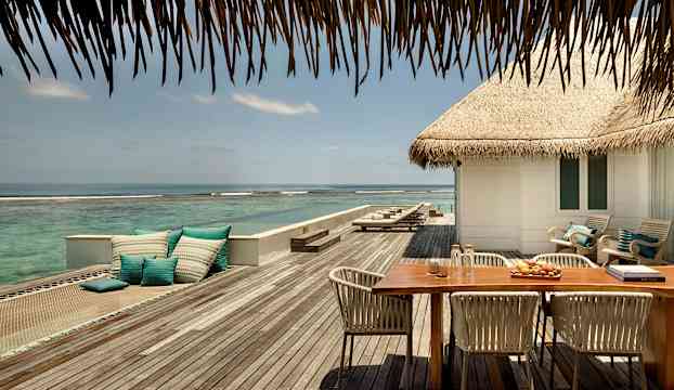 Utsikt över en terrass med bord, stolar och kuddar intill havet. (AI-genererad text)