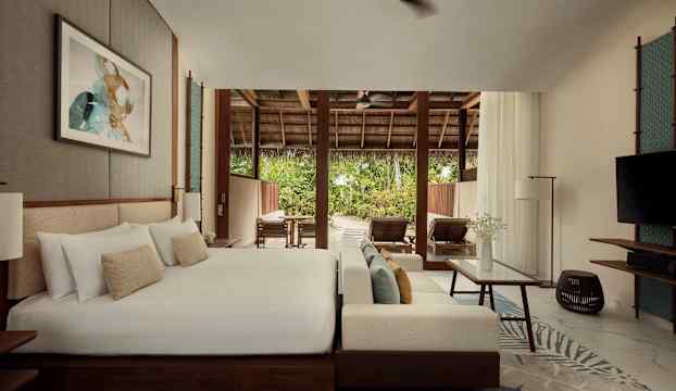 Ett hotellrum med en stor säng, sittgrupp och öppning mot en terrass med solstolar och grönska. (AI-genererad text)