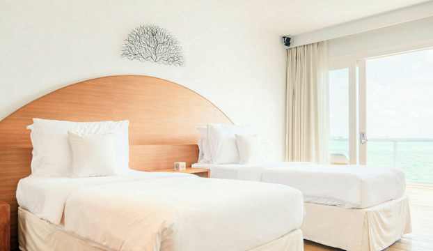 Två separata enkelsängar med vita sängkläder i ett ljust rum med havsutsikt. (AI-genererad text)