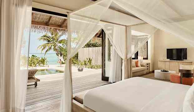 En ljus hotellrum med himmelssäng och utsikt över en terrass, pool och hav. (AI-genererad text)