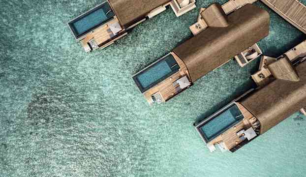 Flygbild av lyxiga villor med privata pooler över klart turkost vatten. (AI-genererad text)