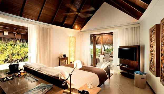 Ett sovrum med högt trätak, säng, skrivbord, och öppning mot veranda. (AI-genererad text)