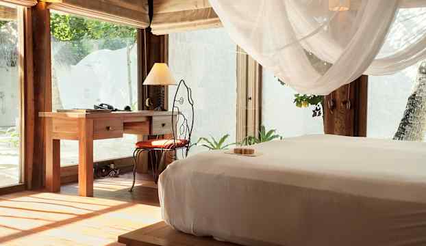 Ett sovrum med trämöbler, inklusive en säng med vit sängklädsel och ett skrivbord med en lampa. (AI-genererad text)