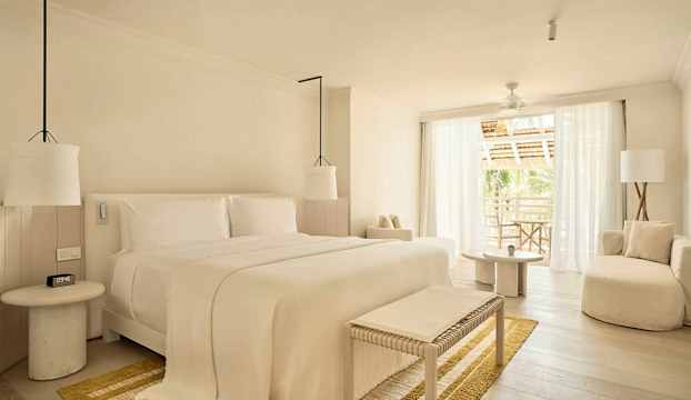 Ett ljust och stilrent sovrum med stor säng, sittmöbler och balkong med utsikt. (AI-genererad text)