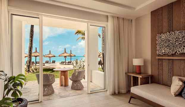 Ett hotellrum med utsikt över en uteplats som leder till en strand med parasoller och solstolar. (AI-genererad text)