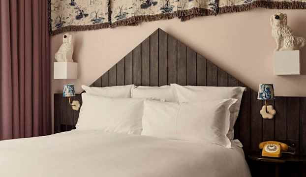 En säng med vita sängkläder, en mörk sänggavel och inredningsdetaljer som dekorativa lampor och keramiska hundstatyer. (AI-genererad text)