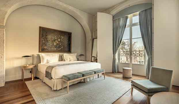 Ett elegant hotellrum med en stor dubbelsäng, sittmöbler och ett stort fönster med gardiner. (AI-genererad text)