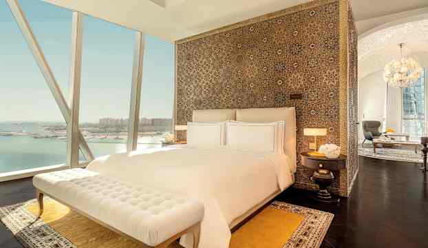 Lyxigt sovrum med utsikt över havet, stor säng med vita lakan, dekorativ huvudgavel och elegant inredning. (AI-genererad text)