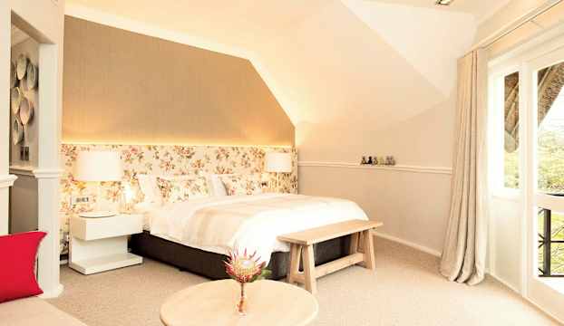 Ett ljust sovrum med blommigt huvudgavel, stor säng och fönster med gardiner. (AI-genererad text)