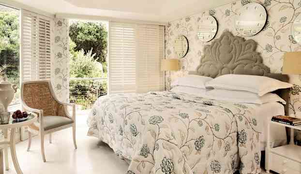 Ett ljust sovrum med ett mönstrat överkast, dekorerade väggar och stora fönster som släpper in naturligt ljus. (AI-genererad text)