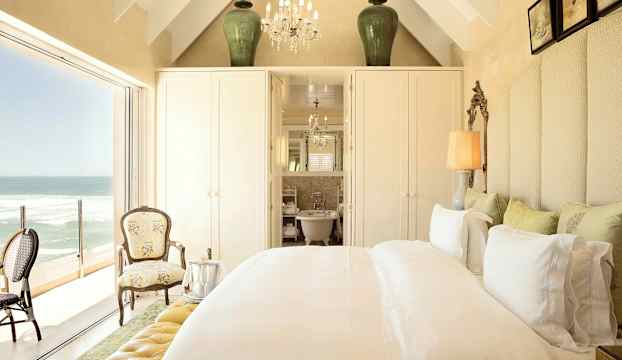 Ett elegant sovrum med havsutsikt, möbler inkluderar en säng, två stolar, och detaljerad inredning. (AI-genererad text)