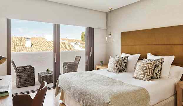 Bild på ett hotellrum med dubbelsäng, dekorerade kuddar och en terrass med sittmöbler. (AI-genererad text)