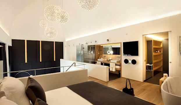 Ett modernt hotellrum med en bekväm dubbelsäng, glasväggar till badrummet och stilfull belysning. (AI-genererad text)