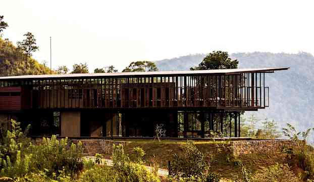 Modern byggnad med glas och träpaneler, omgiven av grönska och berg. (AI-genererad text)