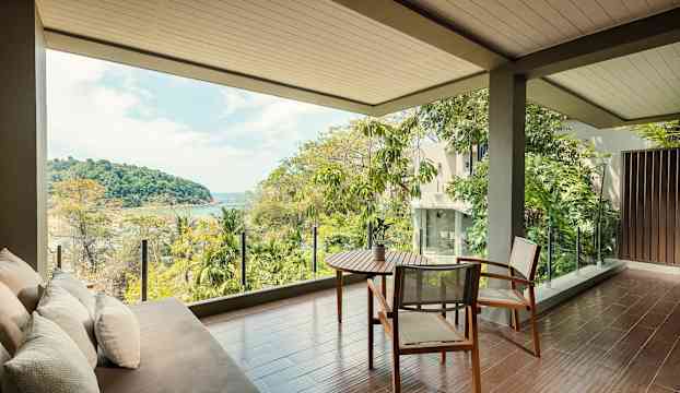 Ett rum med sittmöbler på en terrass med utsikt över grönska och hav. (AI-genererad text)