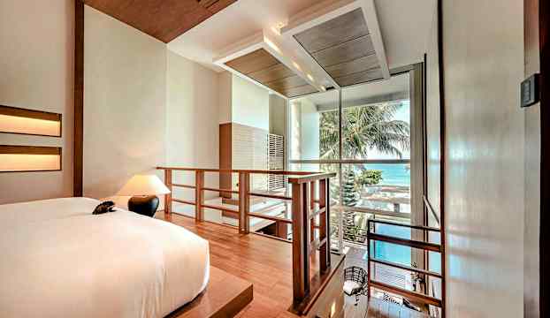 Ett hotellrum med en säng, lampor och en trappa som leder ner mot en balkong med utsikt över havet. (AI-genererad text)