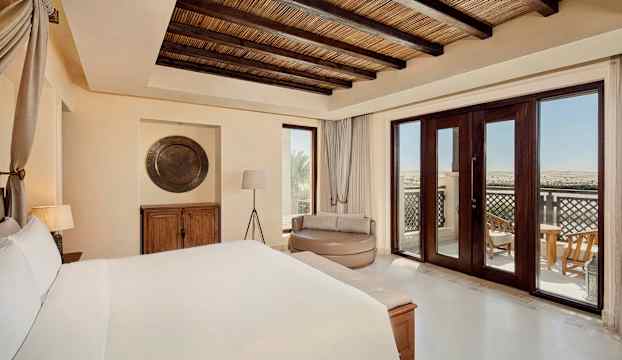 Ett hotellrum med en stor säng, sittmöbler, en trädetaljerad takdesign och en balkong som erbjuder utsikt över landskapet. (AI-genererad text)