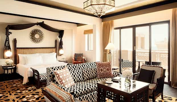 Ett elegant hotellrum med en säng, sittgrupp och balkong. (AI-genererad text)