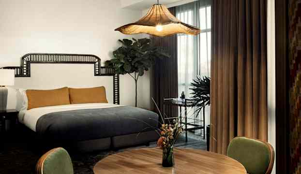 Ett sovrum med en stor säng, en rund träbord med vas med blommor, och fönster med gardiner. (AI-genererad text)