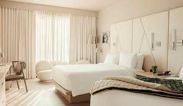 Ett hotellrum med två sängar, en stol och ett fönster med vita gardiner. (AI-genererad text)